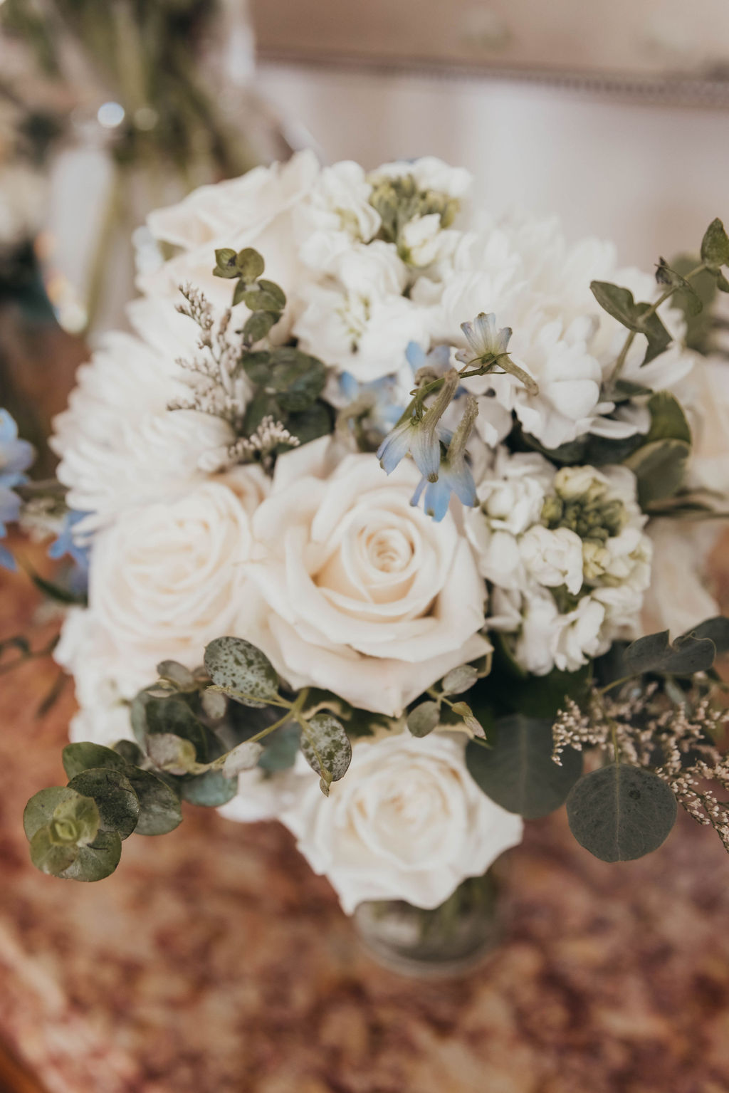 A bouquet of white roses and hydrangeas with greenery accents and a hint of blue flowers, artistically arranged on a table.