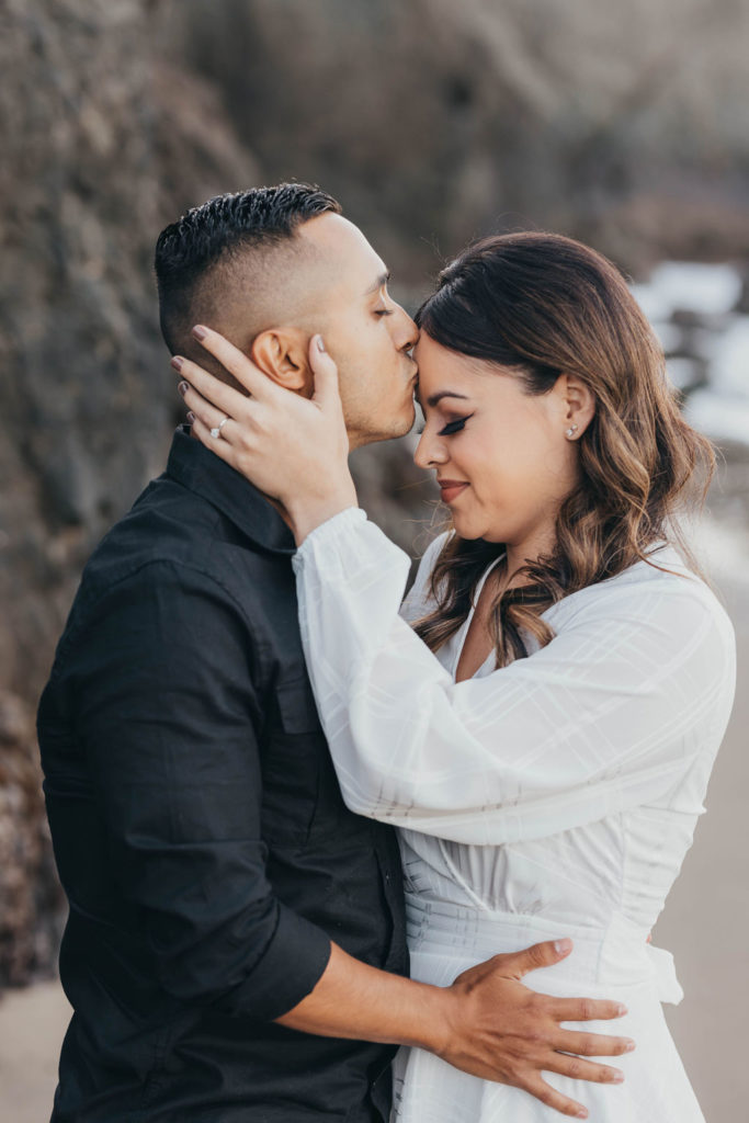 Man kissing womens forhead during beach engagement