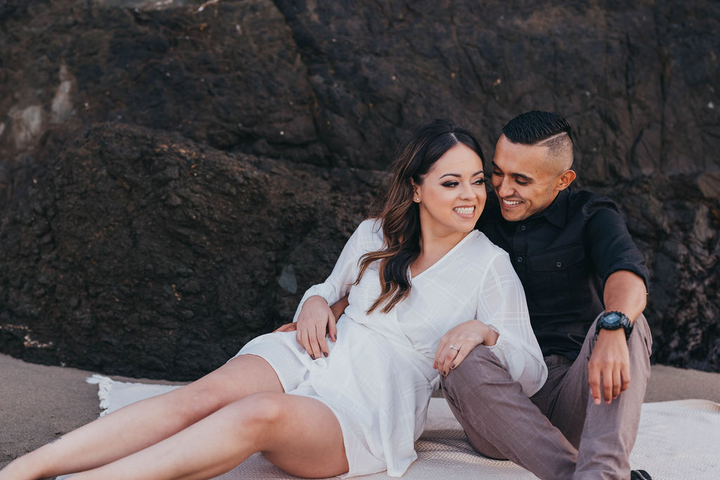 man and woman sitting on the beach for engagement photos