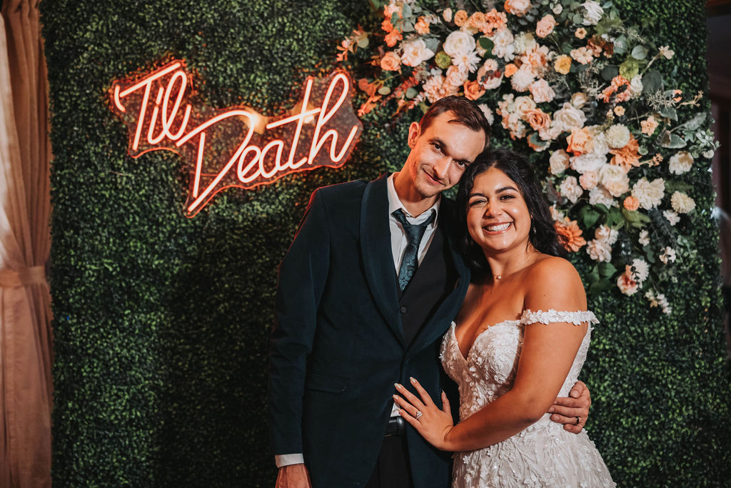 Bride and groom posing in front of neon sign that says "til death"