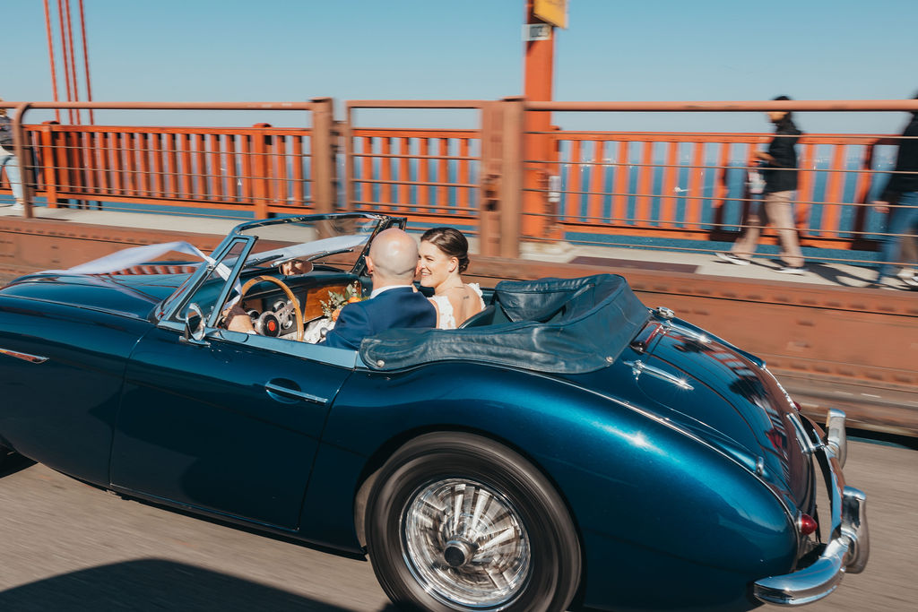 Bride and groom driving over the Golden Gate Bridge in a vintage blue car