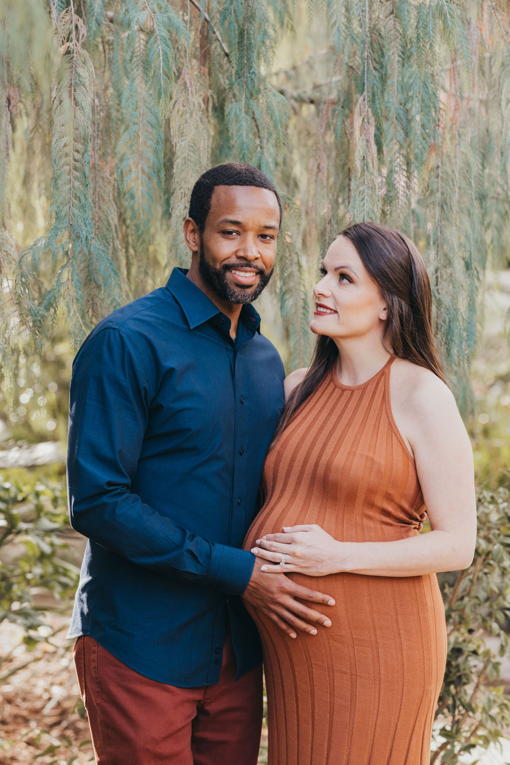 A couple expecting a baby standing together in a garden, with the woman cradling her pregnant belly at their spring maternity photos