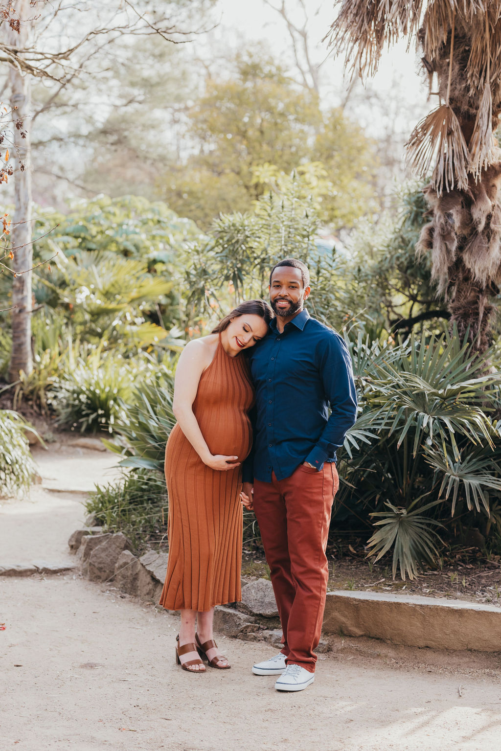 A couple expecting a baby standing together in a garden, with the woman cradling her pregnant belly at their spring maternity photos