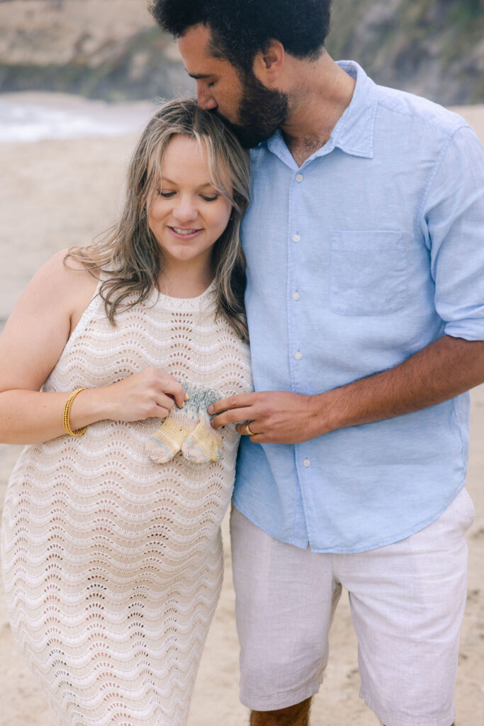 Maternity portrait of Nina smiling while holding her baby bump on the quiet beach 
