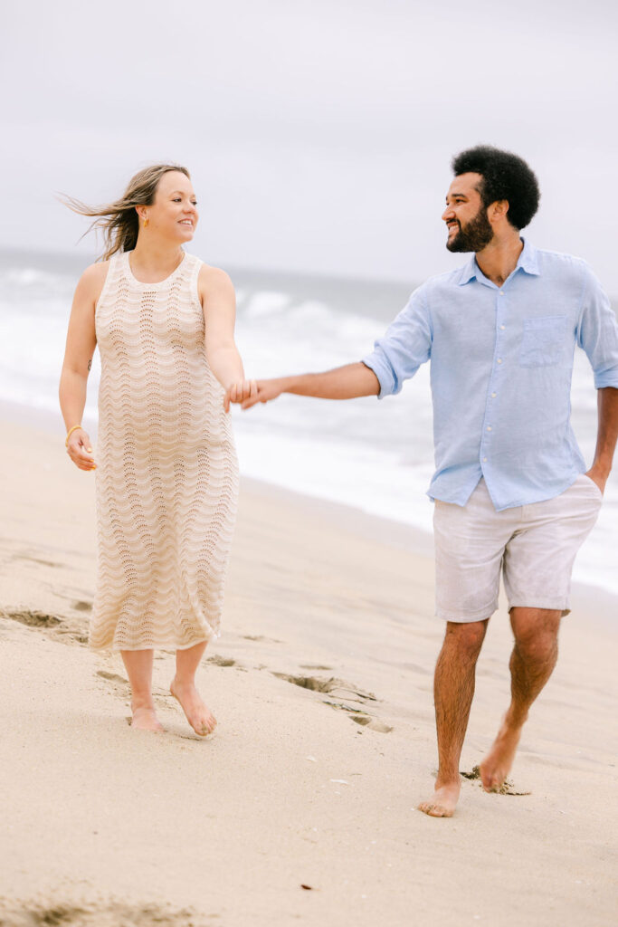 Maternity portrait of Nina smiling while holding her baby bump on the quiet beach 
